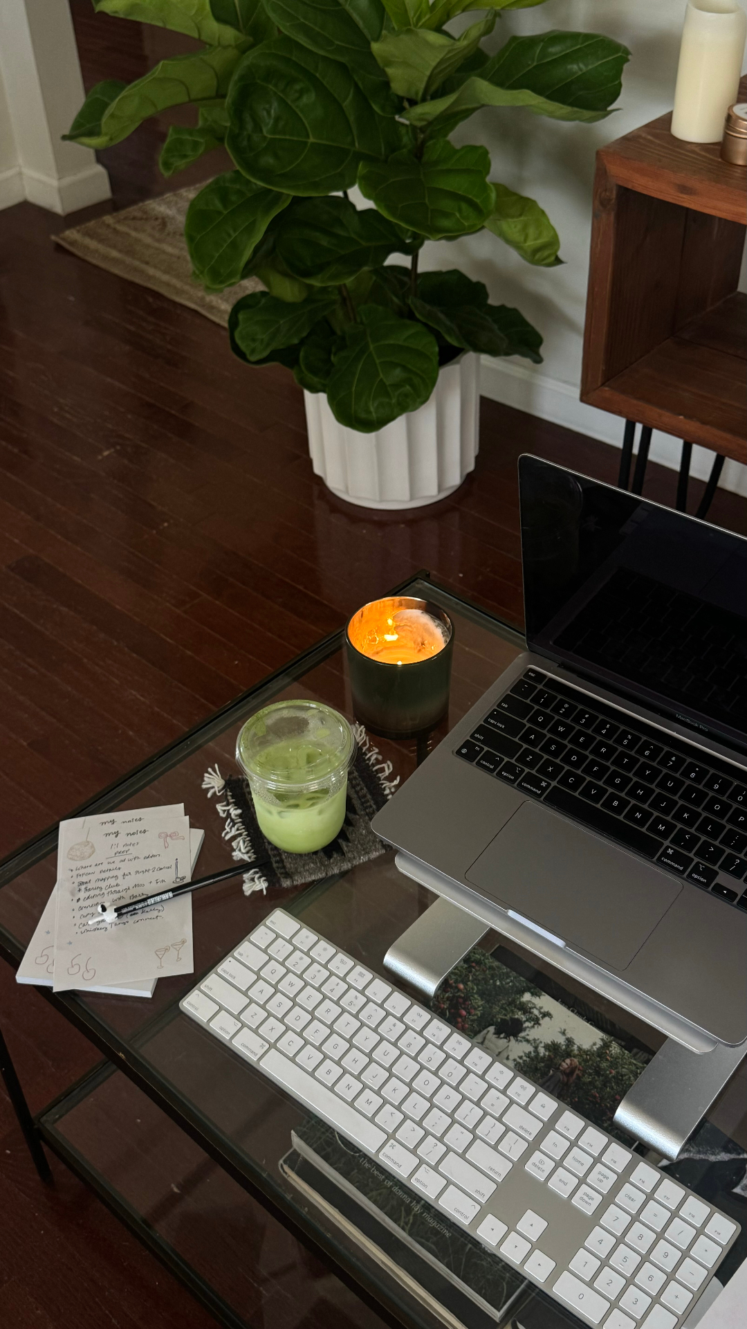 A cozy workspace with a laptop, candle, matcha, and handwritten notes